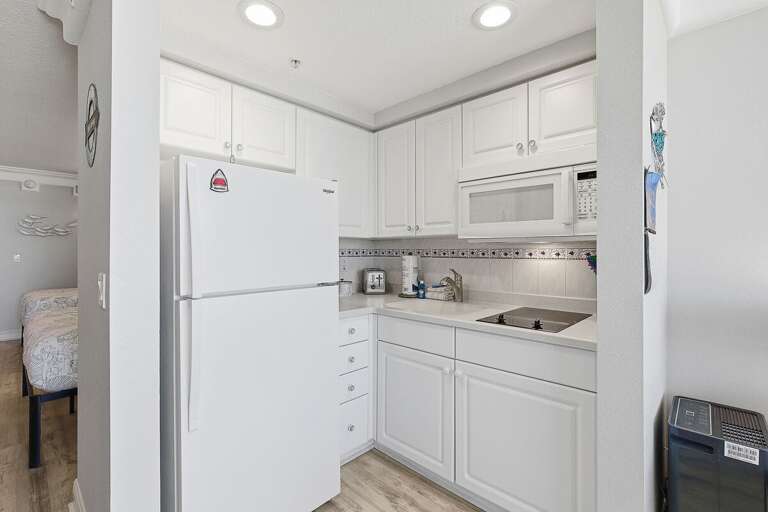 Bright and efficient beach stay kitchenette featuring full-size fridge, microwave, cooktop, and ample cabinetry. Perfect for preparing meals after a day at the beach in your relaxing coastal retreat.