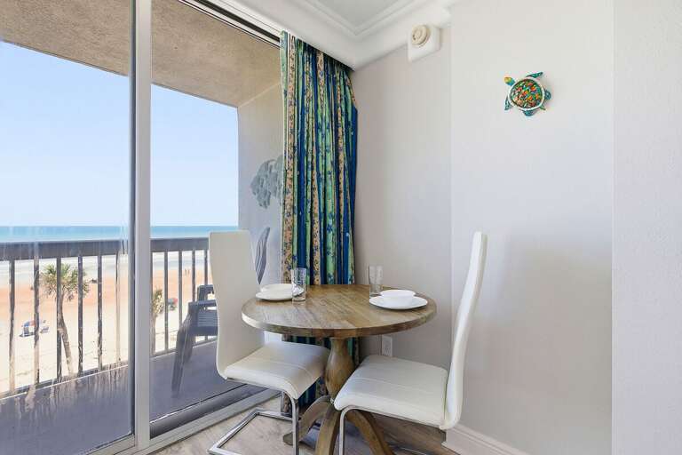 Enjoy meals with a view in this cozy dining nook overlooking the beach. Floor-to-ceiling glass doors open to a private balcony, making it the perfect spot for a relaxing beach stay by the ocean.