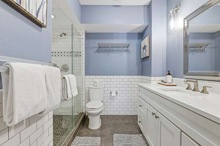 Refresh during your beach stay in this bright coastal bathroom featuring a walk-in shower, clean white tile, and modern vanity. A stylish, relaxing space to unwind after a day at the beach.