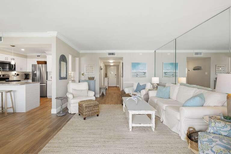 Enjoy a stylish beach stay in this bright coastal condo featuring an open living area, comfortable seating, mirrored accents, and a modern kitchen perfect for relaxing vacations by the shore.
