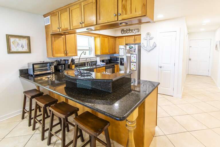 Kitchen bar with dark granite countertops, honey wood cabinets, and four wooden stools on tiled floor.