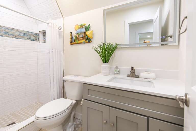 Bathroom with gray shaker vanity, under-mount sink, hex tile floor, and walk-in shower with mosaic tile accent.