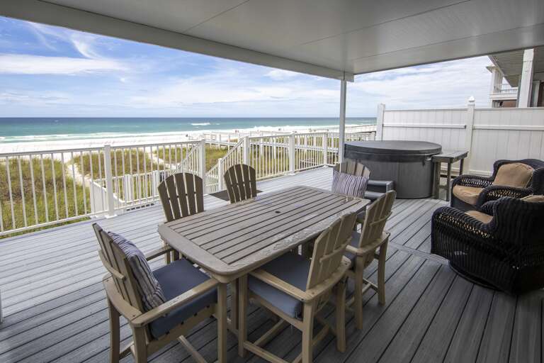 Gray composite deck under covered roof with cushioned wicker chairs, round hot tub, and ocean views beyond white railing.