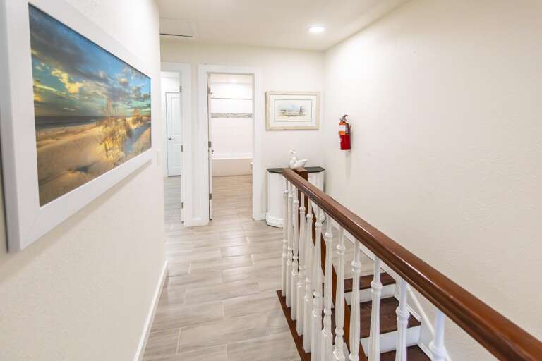 Hallway with wood-look tile flooring, white walls, a coastal print, and a wooden banister leading downstairs.