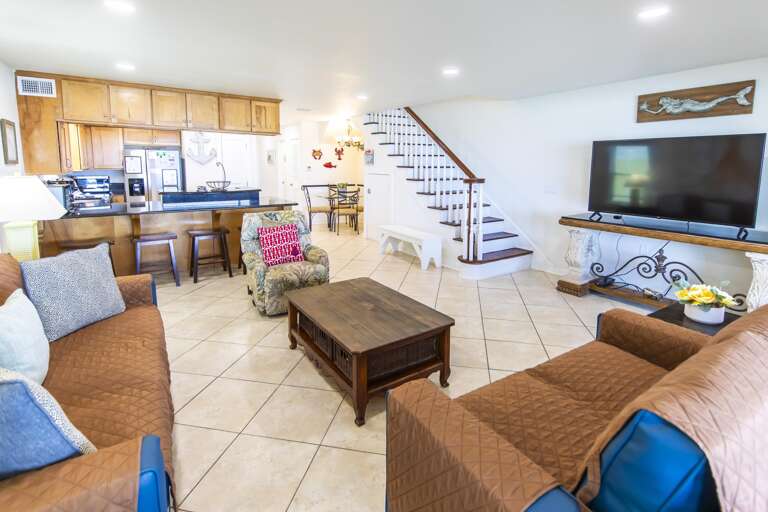 Living area with tiled floors, floral recliner, wooden coffee table, and flat-screen TV on ornate console.