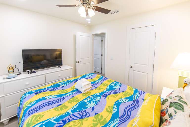White dresser topped with flat-screen TV and tropical figurine contrasts with multicolored bedspread in bedroom.