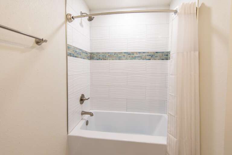 Bathroom tub with white wave-textured tiles accented by a horizontal band of blue mosaic glass tiles.