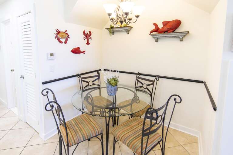Glass-top dining table with wrought iron chairs featuring striped cushions and coastal wall decor.