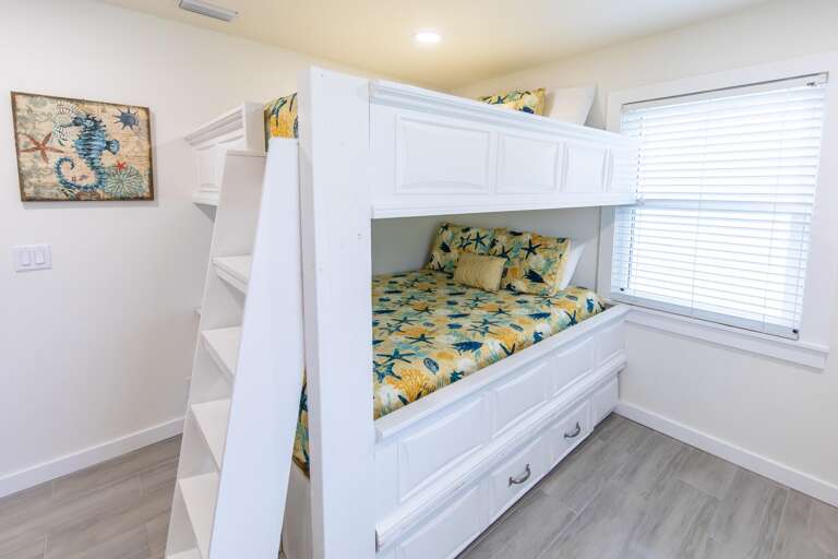 White wooden bunk beds with under-bed drawers and sea-themed bedding sit beside a window with blinds.
