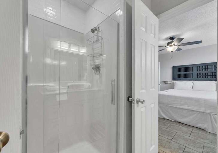 Bright, modern bathroom with spacious glass shower and cozy bedroom glimpse