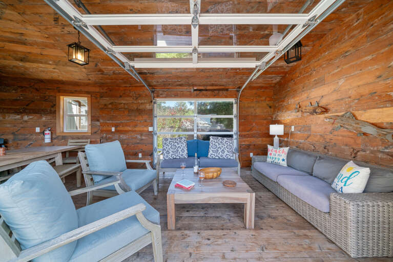 Outdoor living space with covered lounging furniture, streaming TV, dining area, open to back yard with BBQ. 