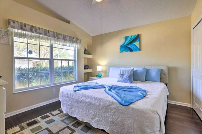 A queen-sized bed, a large window, and decorative shelves. The room has a calming color scheme with blue and white accents. A queen-sized bed, a large window, and decorative shelves. The room has a calming color scheme with blue and white accents.