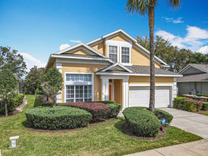 Inviting yellow toned home with double gables, sculpted hedges, and a pristine white garage set against a clear blue sky. Inviting yellow toned home with double gables, sculpted hedges, and a pristine white garage set against a clear blue sky.