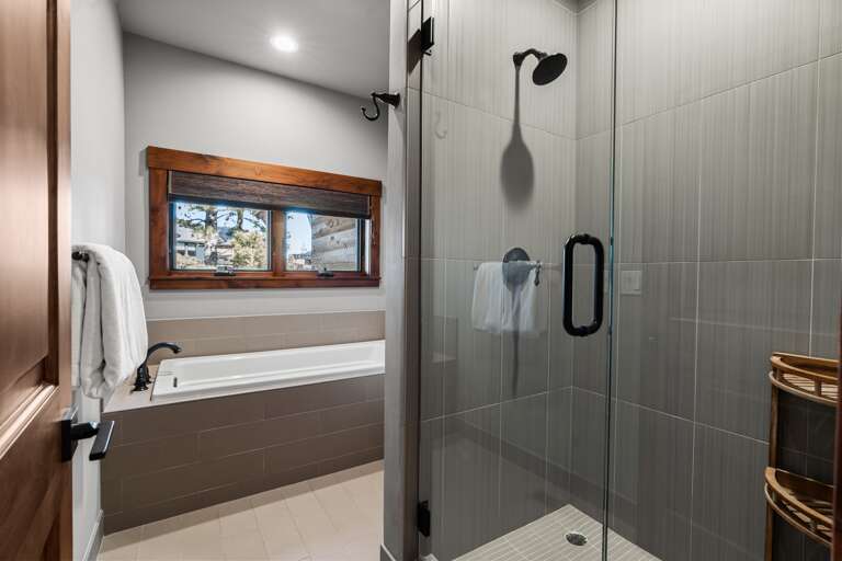 This bathroom features dual vanities, a soaking tub, and a spacious walk-in shower, offering both style and functionality. Thoughtfully stocked with shampoo, conditioner, and body wash for a comfortable and convenient stay.