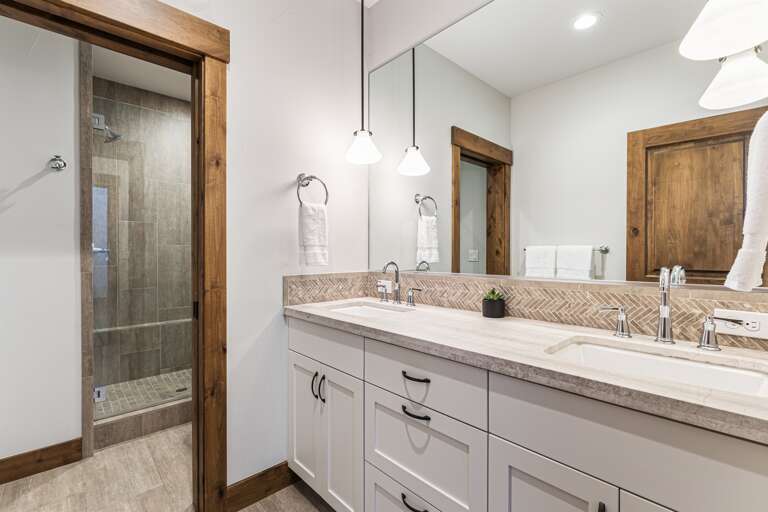 This bathroom features dual vanities and a spacious walk-in shower, providing both style and functionality. Thoughtfully stocked with shampoo, conditioner, and body wash for a comfortable stay.
