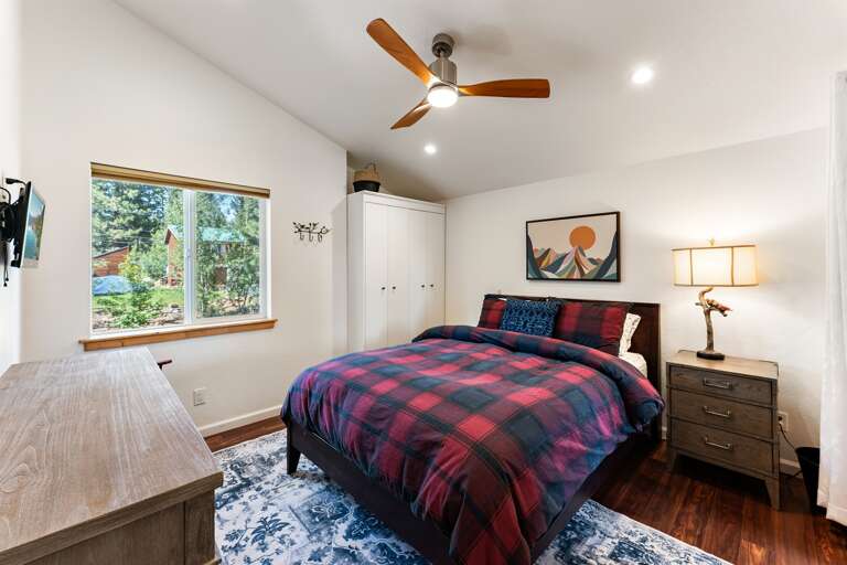 The upstairs bedroom features a queen bed, a ceiling fan, and access to the upper deck with fresh mountain views. It also connects to the Jack and Jill bathroom for added convenience.