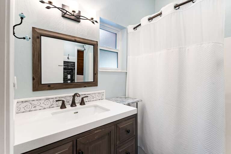 The upstairs bedroom features a queen bed, a ceiling fan, and access to the upper deck with fresh mountain views. It also connects to the Jack and Jill bathroom for added convenience.