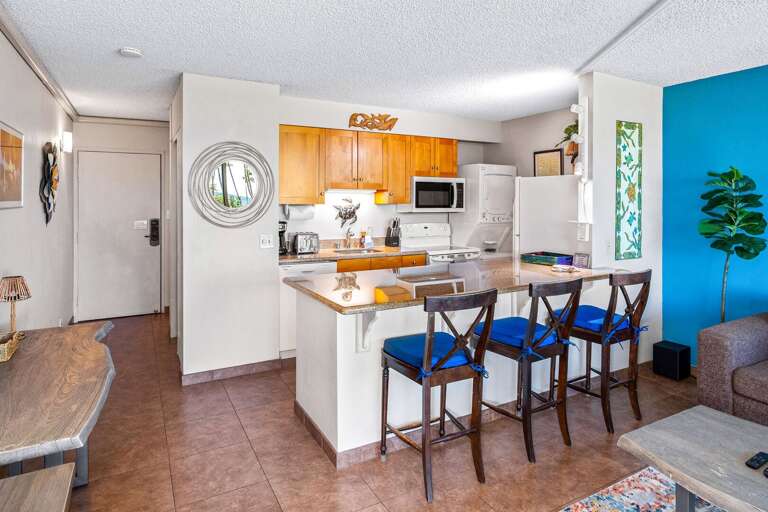 Open Kitchen With Bar Stools, Wooden Cabinets, Blue Accent Wall, And Plant