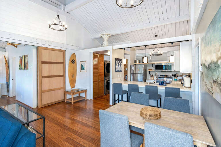 Open-plan Space With Surfboard, Sleek Kitchen, Wooden Floors, And Dining Table