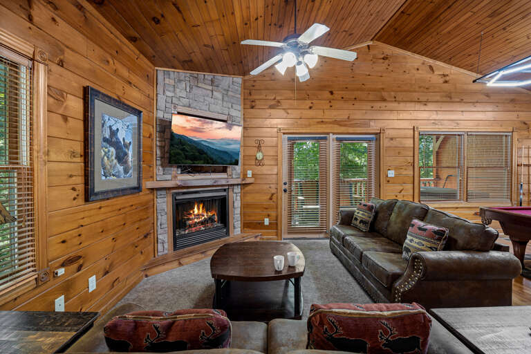 Wood-walled Room With Fireplace, Ceiling Fan, And Furniture Facing Glass Doors