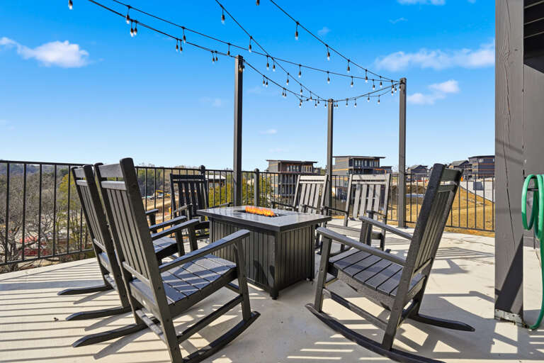 Rocking Chairs Encircle A Central Table Under String Lights On A Sunlit Balcony