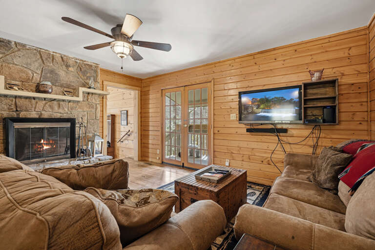 Wood-paneled Living Room With Fireplace, Plush Sofas, TV, And A Ceiling Fan
