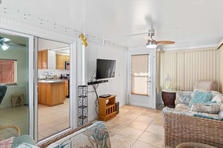 Brightly Lit Vacation Rental Living Room With Kitchen View, Featuring Wicker Furniture And Ceiling Fan