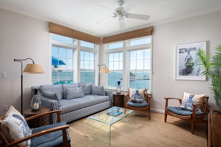 Living Room With Large Windows Overlooking Sea, Striped Sofa, And Wooden Chairs