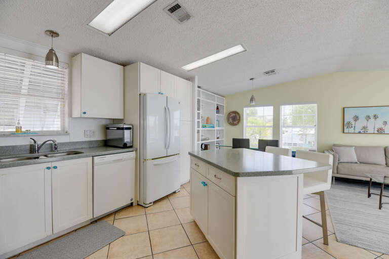 Bright, Breezy Kitchen Space With White Cabinets And Tiled Floor, Leading Into Living Area