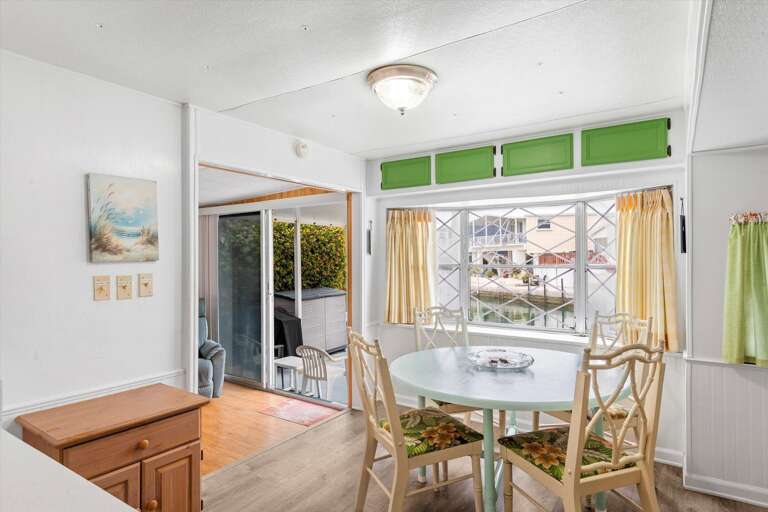 Bright Dining Space With Glass Table, Green Accents, Leading To Light-filled Balcony