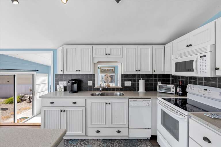 Spacious Kitchen, White Cabinets, Black Countertops, Sea Glimpse Through Door