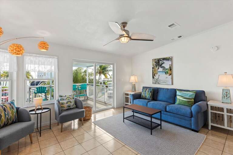 Bright Breezy Room With Blue Sofas, Ceiling Fan, And Sliding Doors To Balcony
