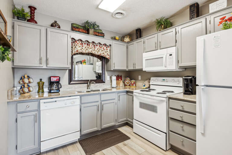 Kitchen Space Sporting White Cabinetry And Appliances With A Tile Floor