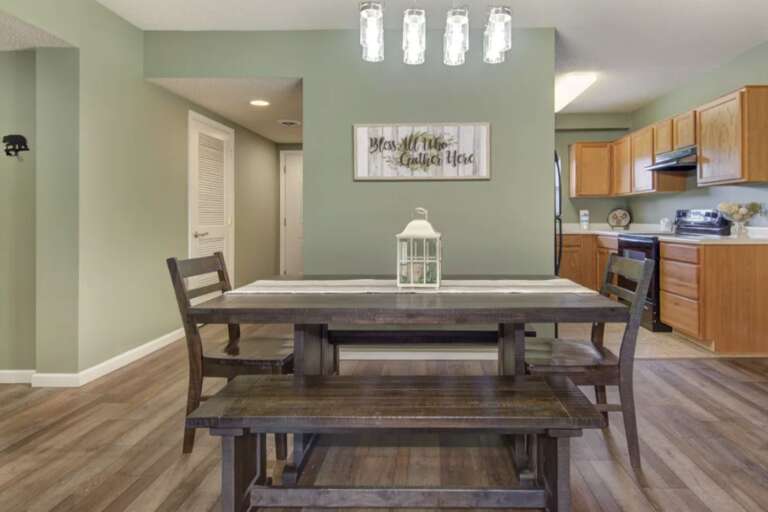 Wooden Table And Chairs In A Green Room With Kitchen View