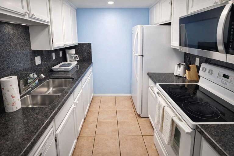 Compact Kitchen With White Cabinets, Granite Counters, Fridge, Stove, And Microwave