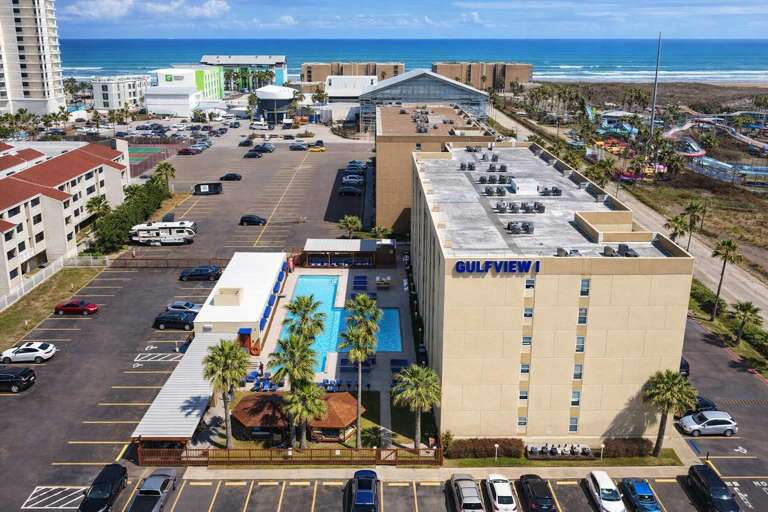Seaside Structure With Pool, Palm Trees, Parking Lot, Ocean Backdrop