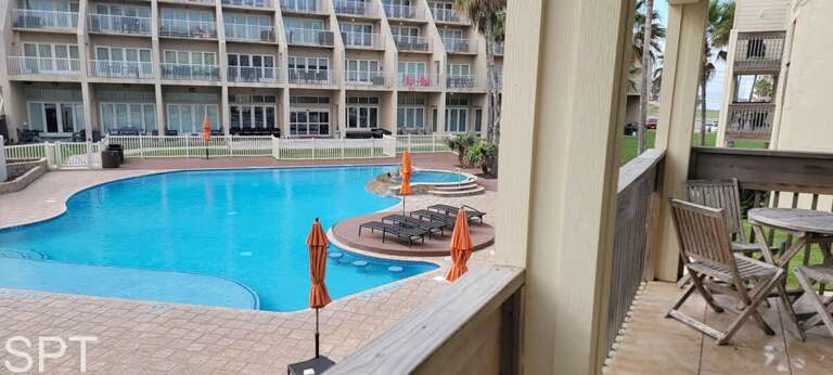 Balcony View Of A Blue Pool Between Buildings With Chairs And Umbrellas