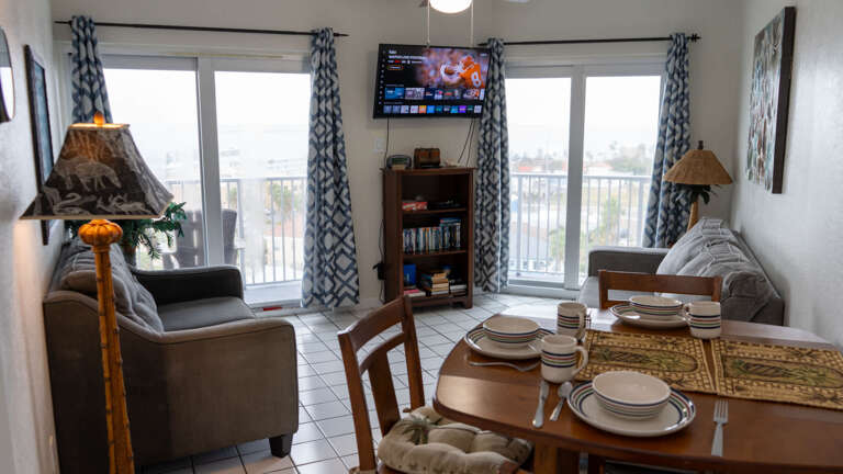 Interior View Of A Room With A Dining Table Set, Sofa, Television, And Balcony Doors