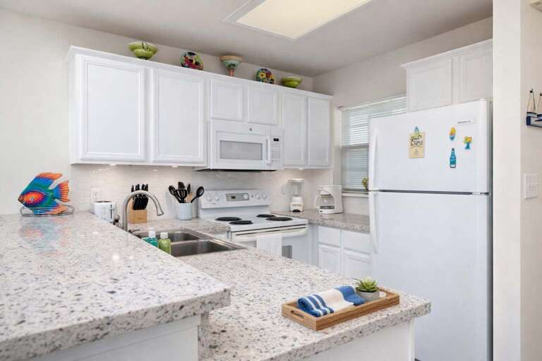 White Kitchen With Granite Countertop, Fridge, And Stove