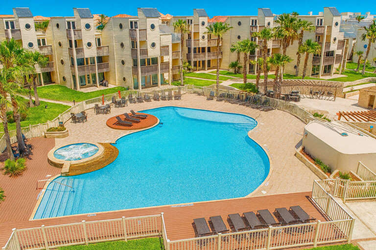 Curved Pool, Palm Trees, Sunlit Loungers, Beige Buildings