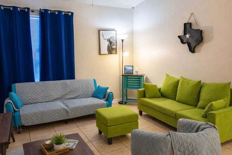 Living Room With Green Sofas, Blue Curtains, And Texas Wall Art