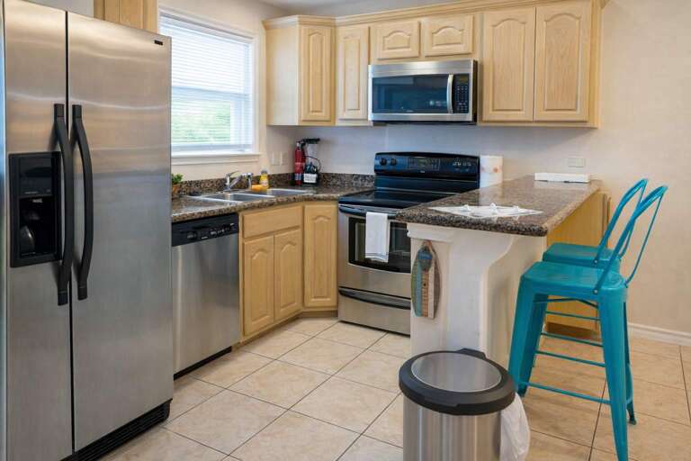 Kitchen With Stainless Steel Appliances, Wooden Cabinets, And Turquoise Stools