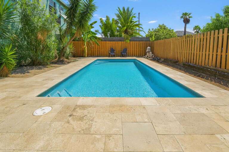 Sunlit Swimming Pool Surrounded By Palm Trees And Wooden Fence