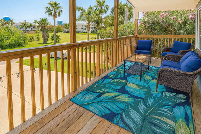 Balcony View With Palm Trees, Vibrant Rug, And Wicker Seating