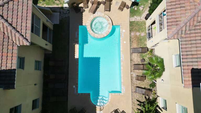 Aerial View Of A Turquoise Pool Surrounded By A Sunlit Patio And Palms