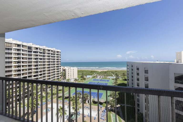 View From Vacation Rental Balcony Showcasing Ocean, Buildings, And Blue Sky