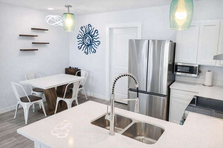 Kitchen With Stainless Steel Fridge, Double Sink, Dining Table, And Wall Art