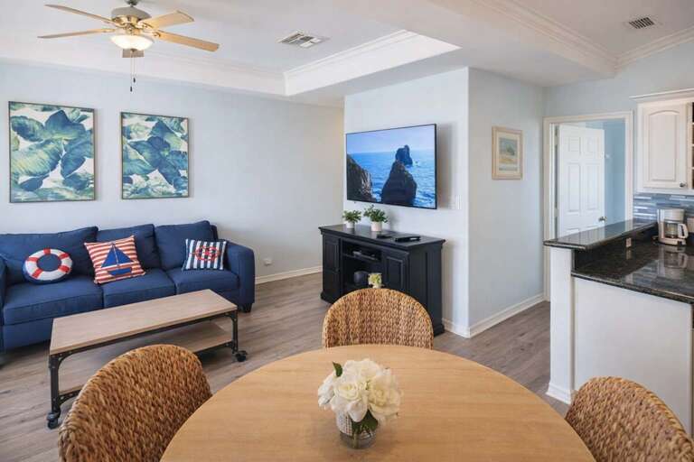 Living Room With Blue Sofa, TV, Round Table, Wicker Chairs, And Wall Art