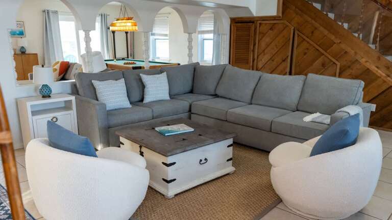 Spacious Seaside Vacation Rental Living Area With Large Gray Sectional Sofa And Plush White Chairs