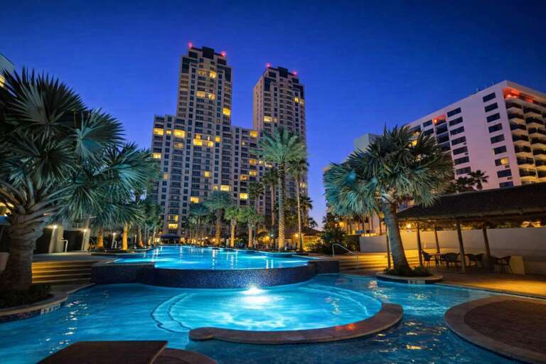 Palm-lined Pool Beneath Towering Buildings At Twilight